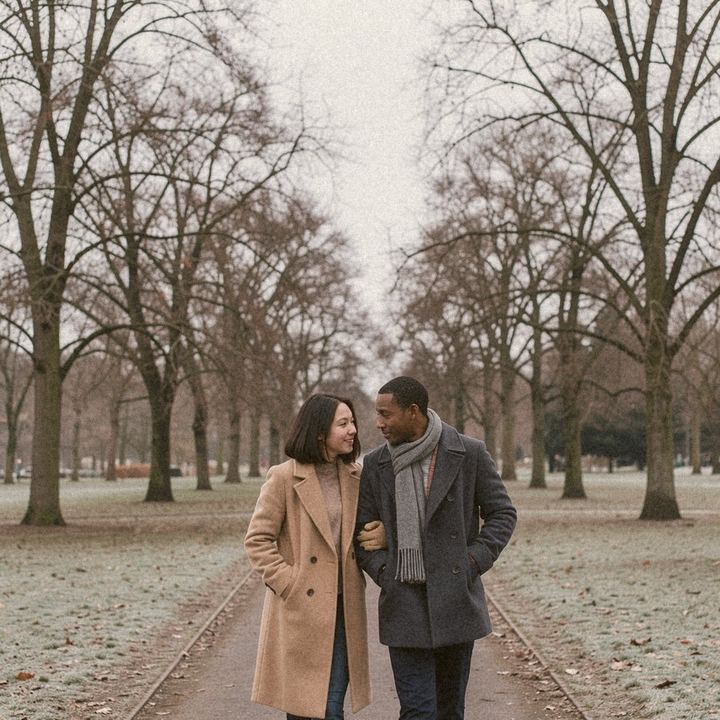 AI-generated example with fictional people: A couple in wool coats walking a frosty park path under bare trees on an overcast day, no snow